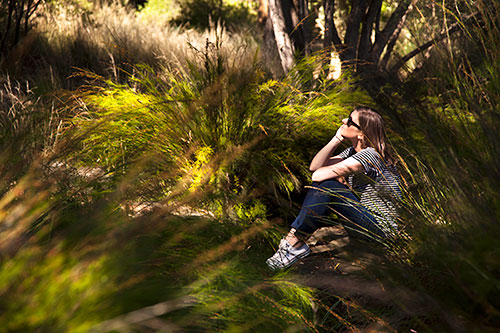Student pictured in the sun sitting in our Burnley Native Garden surrounded by native herbs and grasses.