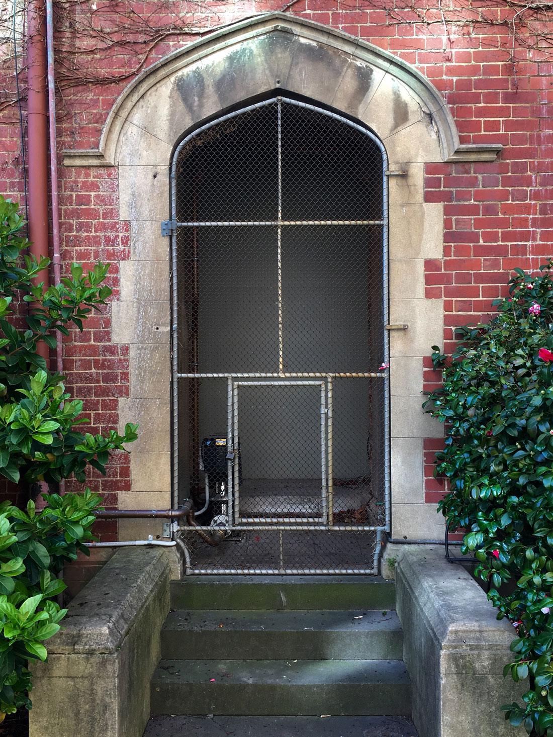 Photo of a brick doorway with stairs leading up. The doorway is fitted with a steel frame and a wire gate.