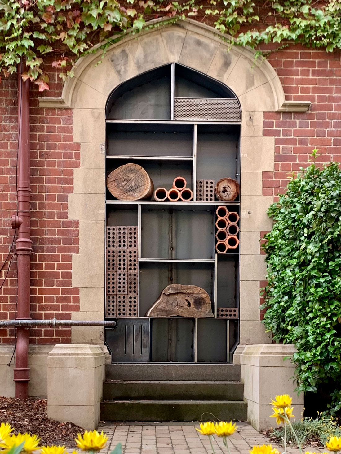 Photo of a brick doorway with stairs leading up. The doorway is fitted with a steel frame divided into sections with a few larger logs and bricks sitting in some sections