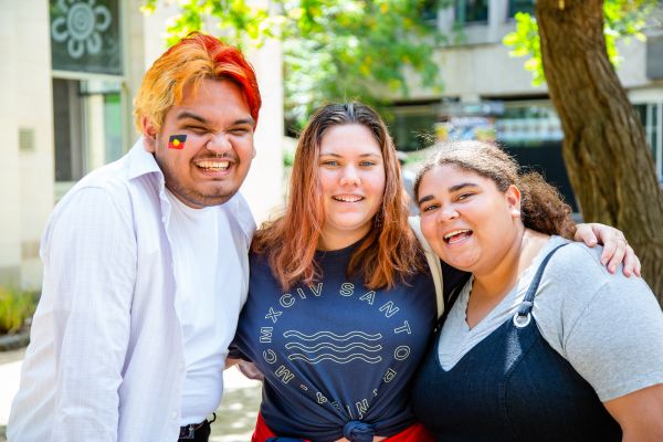 Three indigenous students smiling in embrace